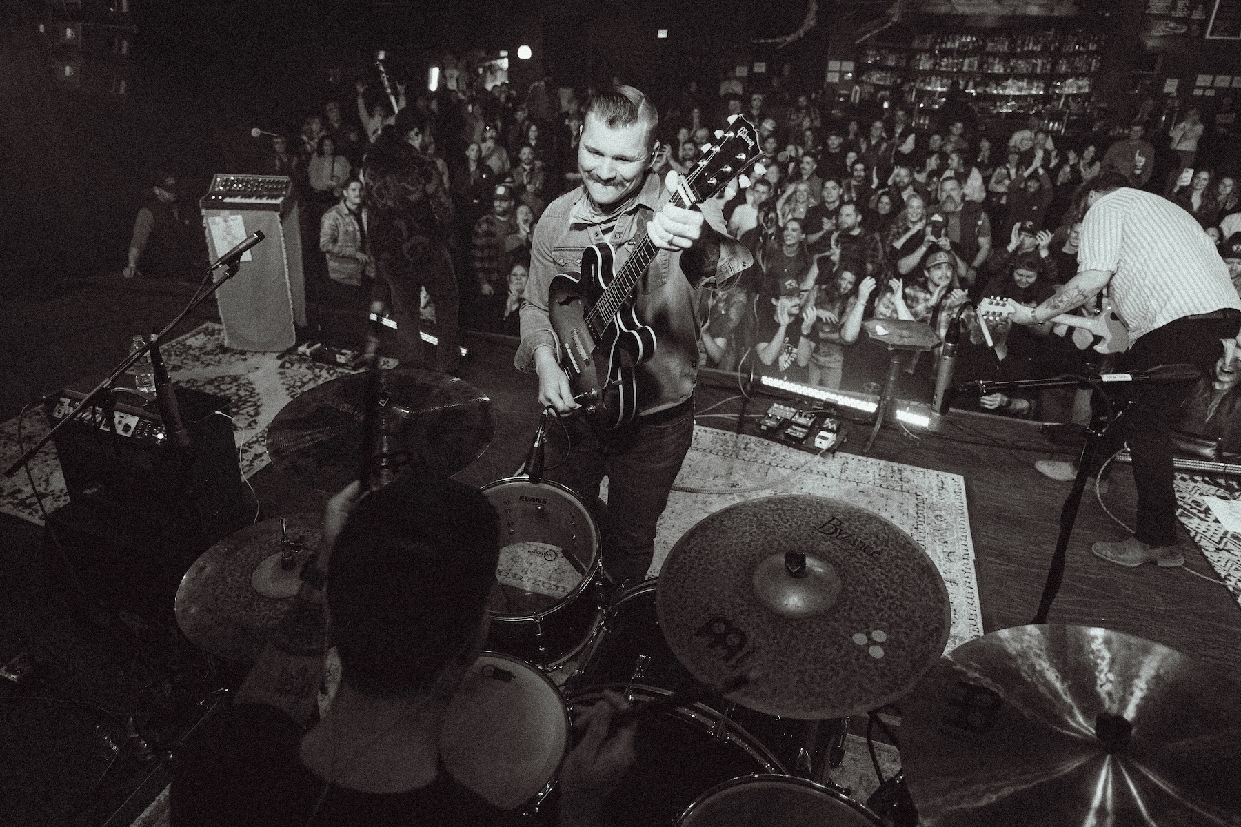 Auto-generated description: A band performs energetically on stage in front of an enthusiastic crowd in a black-and-white photograph.