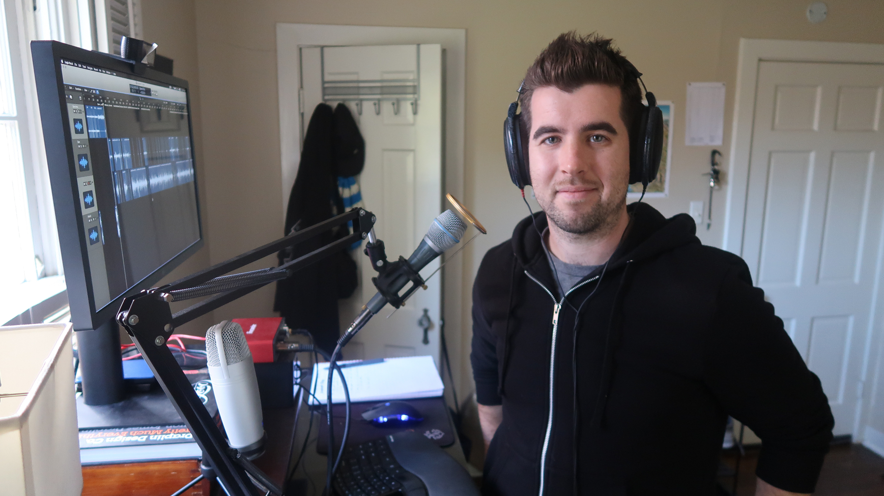 Aaron Dowd standing at his desk with a Shure Beta 87a microphone and Logic Pro open on a computer monitor